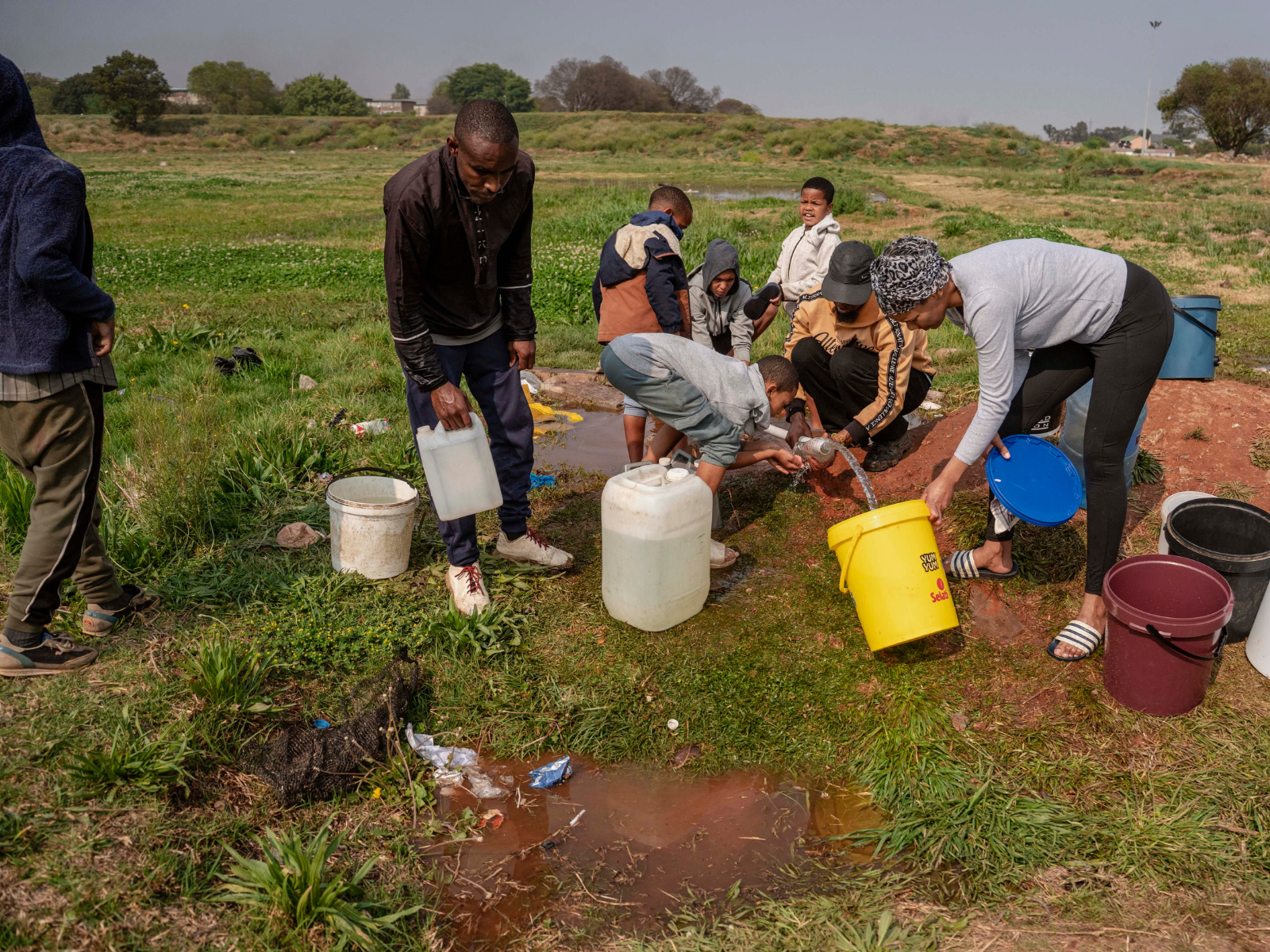 People gather water at an abandoned sports field where a pipe gushes water