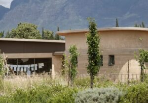 A simple building with windows set up high near the roof in a field with mountains in the background