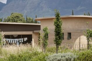 A simple building with windows set up high near the roof in a field with mountains in the background