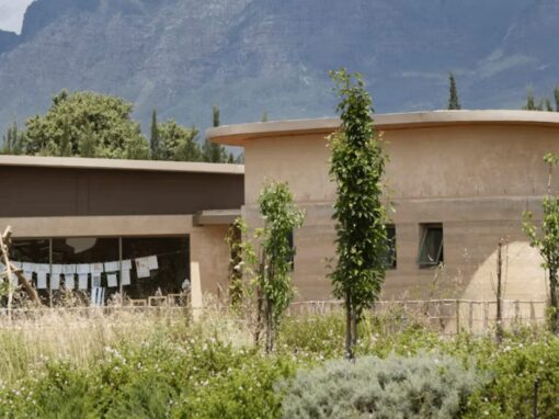 A simple building with windows set up high near the roof in a field with mountains in the background