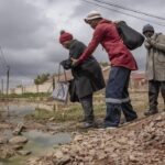 An elderly woman is helped across a stream of sewage in Letsopa near Ottosdal in the North West province