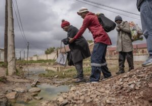 An elderly woman is helped across a stream of sewage in Letsopa near Ottosdal in the North West province