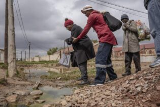 An elderly woman is helped across a stream of sewage in Letsopa near Ottosdal in the North West province
