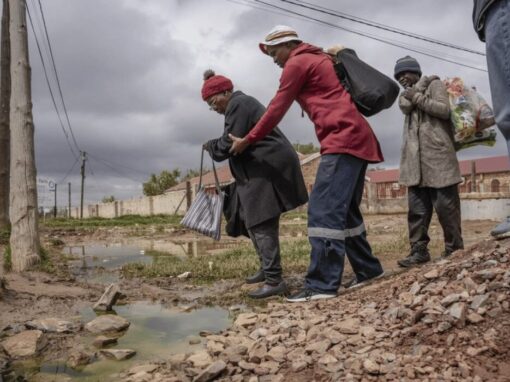 An elderly woman is helped across a stream of sewage in Letsopa near Ottosdal in the North West province