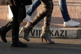 Low-level view of legs and feet of people walking along a street; painted street name visible on the kerb