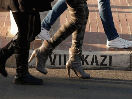 Low-level view of legs and feet of people walking along a street; painted street name visible on the kerb