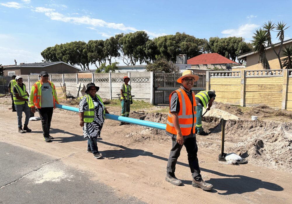 four people carrying a plastic pipe to replace wastewater pipe