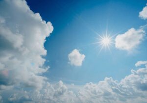 sun in a blue sky surrounded by clouds