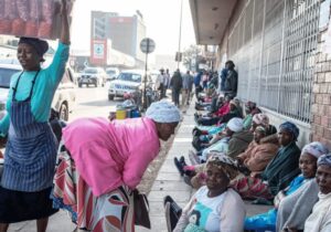 Elderly women sit in a row on a city pavement