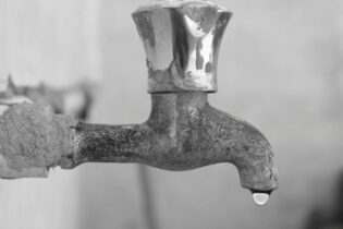 leaking tap with a droplet of water in greyscale